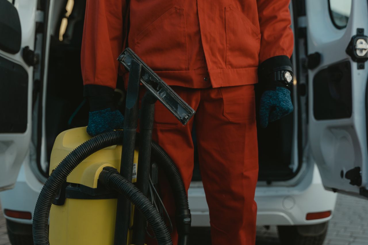 about-us-01 A professional cleaner in a red uniform holding a vacuum near a van, ready for service.