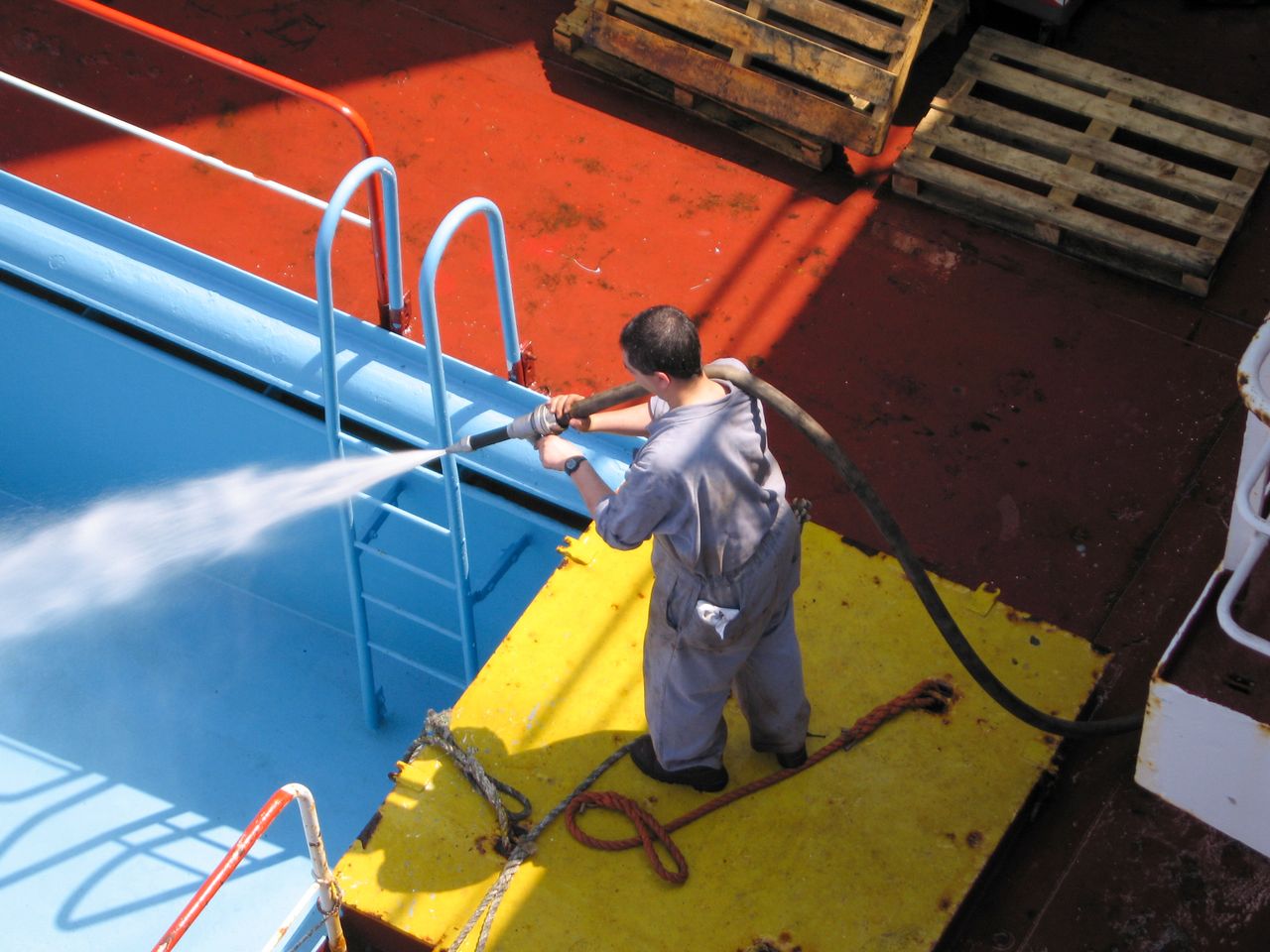 about-us-02 A worker using a high-pressure hose to clean the deck of a ship, showing industrial processes.